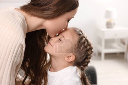 Glückliche Mutter küsst ihre süße Tochter zu Hause