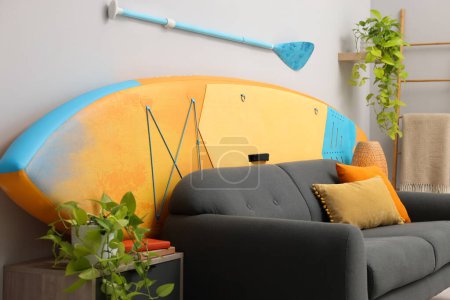 Photo for SUP board, paddle and stylish sofa in living room. Interior design - Royalty Free Image