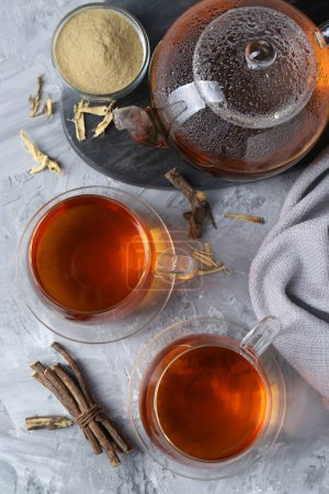 Aromatic licorice tea, dried sticks of licorice root and powder on light gray textured table, flat lay