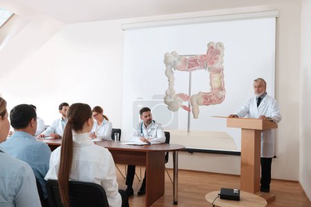 Photo for Lecture in gastroenterology. Conference room full of professors and doctors. Projection screen with illustration of large intestine - Royalty Free Image