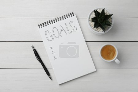 Planungskonzept. Leere Zielliste in Notizbuch, Stift, Kaffee und Zimmerpflanze auf weißem Holztisch, flach gelegt