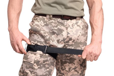 Foto de Soldado en uniforme militar aplicando torniquete médico sobre pierna sobre fondo blanco, primer plano - Imagen libre de derechos