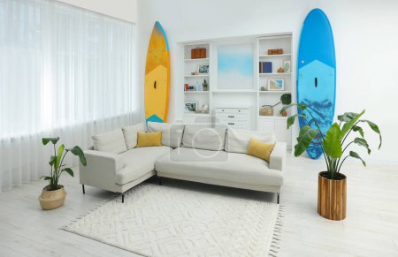 Photo for SUP boards, shelving unit with different decor elements and stylish sofa in room. Interior design - Royalty Free Image