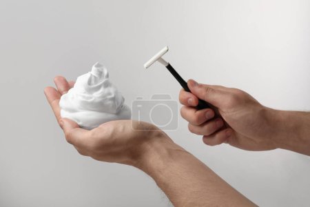 Photo for Man holding shaving foam and razor on light grey background, closeup - Royalty Free Image