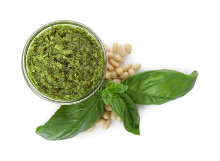 Delicious pesto sauce in bowl, pine nuts and basil leaves isolated on white, top view
