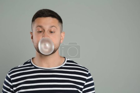 Téléchargez les photos : Beau homme soufflant de la gomme à bulles sur fond gris clair, espace pour le texte - en image libre de droit