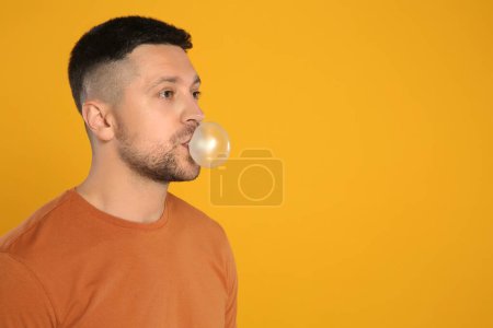 Photo for Handsome man blowing bubble gum on orange background, space for text - Royalty Free Image