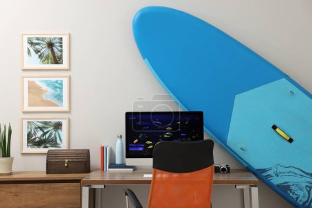 Photo for Stylish workplace with modern computer and SUP board near light wall in room. Interior design - Royalty Free Image
