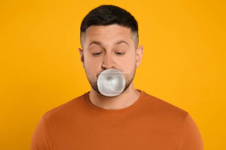 Téléchargez les photos : Bel homme soufflant chewing-gum bulle sur fond orange - en image libre de droit