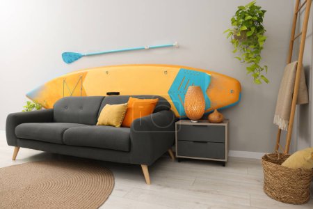 Photo for SUP board, paddle and stylish sofa in living room. Interior design - Royalty Free Image