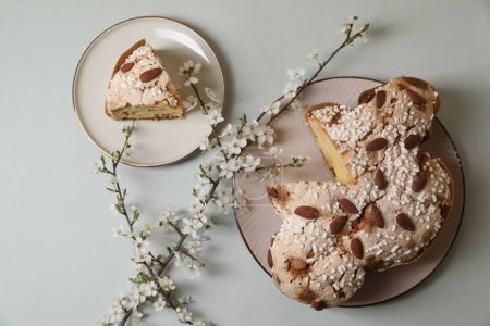 Foto de Platos con corte delicioso pastel de paloma de Pascua italiana (Colomba di Pasqua tradicional) y ramas de flores en la mesa gris claro, la puesta plana - Imagen libre de derechos