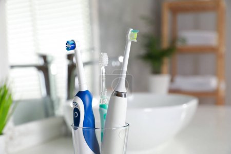 Electric toothbrushes in glass holder indoors, closeup