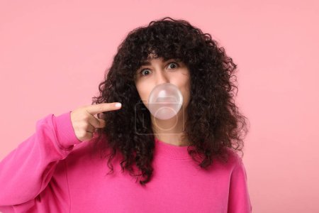 Beautiful young woman blowing bubble gum on pink background