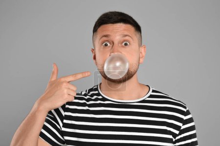 Téléchargez les photos : Homme surpris soufflant de la gomme à bulles sur fond gris clair - en image libre de droit