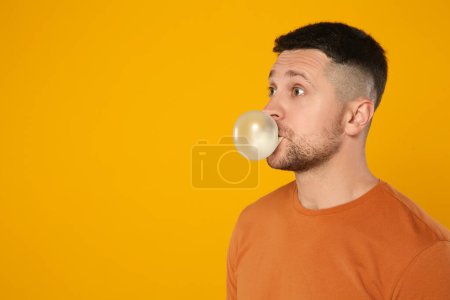 Téléchargez les photos : Homme surpris soufflant de la gomme à bulles sur fond orange, espace pour le texte - en image libre de droit