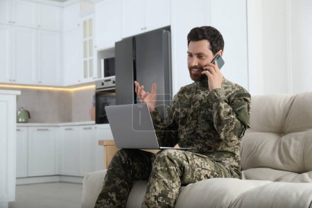 Foto de Soldado con portátil hablando por teléfono en casa. Servicio militar - Imagen libre de derechos