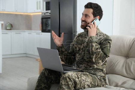 Foto de Feliz soldado con portátil hablando por teléfono en casa. Servicio militar - Imagen libre de derechos