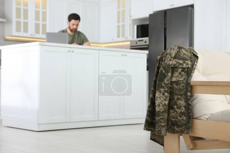 Soldat utilisant un ordinateur portable à la table dans la cuisine, se concentrer sur l'uniforme. Service militaire