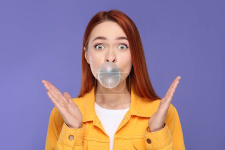 Téléchargez les photos : Femme surprise soufflant chewing-gum bulle sur fond violet - en image libre de droit