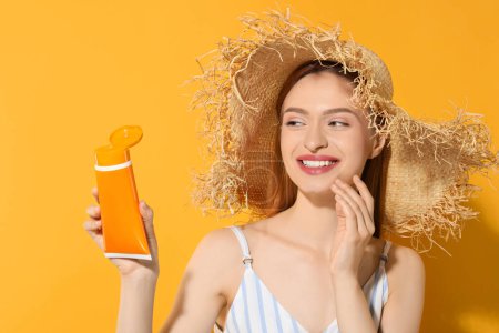 Photo for Beautiful young woman in straw hat holding sun protection cream on orange background - Royalty Free Image