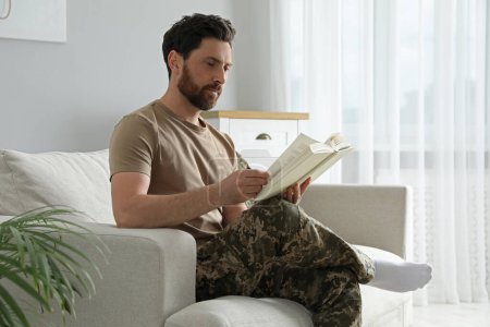 Foto de Soldado leyendo libro sobre sofá blando en sala de estar. Servicio militar - Imagen libre de derechos