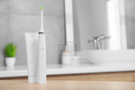 Photo for Electric toothbrush and tube with paste on wooden table in bathroom. Space for text - Royalty Free Image