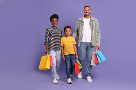 Téléchargez les photos : Shopping en famille. Parents heureux et fils avec des sacs colorés sur fond violet - en image libre de droit