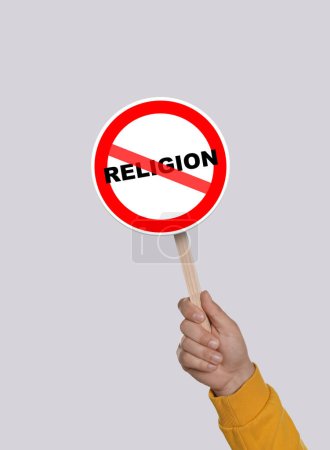 Foto de Concepto de ateísmo. Hombre sosteniendo un cartel de prohibición con la palabra tachada Religión sobre fondo gris claro - Imagen libre de derechos