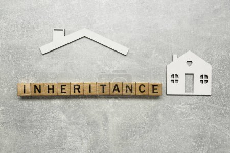 Word Inheritance aus Holzwürfeln und Hausmodell auf grauem Hintergrund, flach gelegt