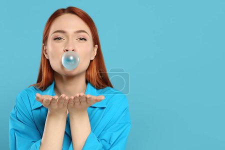 Téléchargez les photos : Belle femme soufflant de la gomme à bulles sur fond turquoise, espace pour le texte - en image libre de droit