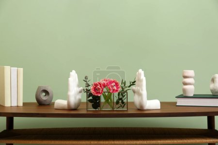 Wooden coffee table with flowers and decor elements near pale green wall indoors. Stylish interior design