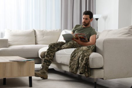 Soldier reading magazine on sofa in living room. Military service