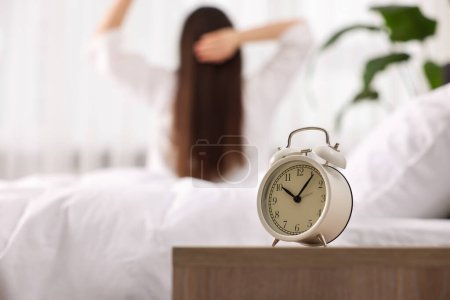 Photo for Alarm clock on nightstand. Woman awakening on bed at home, selective focus - Royalty Free Image