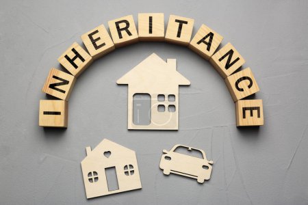 Word Inheritance made with wooden cubes, car and houses models on grey background, flat lay