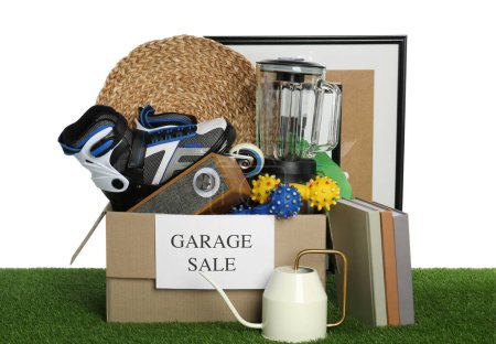 Téléchargez les photos : Boîte avec signe Vente de garage et différentes choses sur l'herbe verte sur fond blanc - en image libre de droit