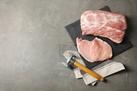 Téléchargez les photos : Schnitzel de cuisine. Côtelettes de porc crues avec maillet à viande sur table grise, plat et espace pour le texte - en image libre de droit