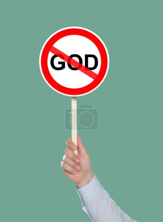 Foto de Concepto de ateísmo. Hombre sosteniendo la prohibición signo con la palabra tachada Dios sobre fondo verde pálido - Imagen libre de derechos