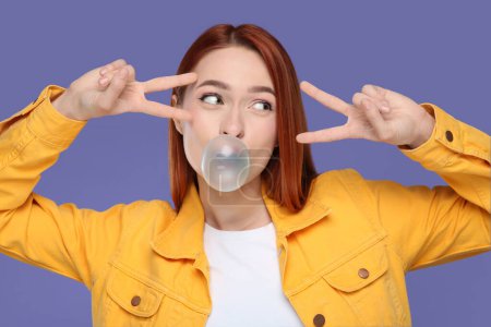 Photo for Beautiful woman blowing bubble gum and gesturing on purple background - Royalty Free Image