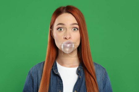 Photo for Surprised woman blowing bubble gum on green background - Royalty Free Image