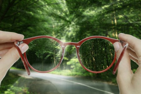 Vision correction. Woman looking through glasses and seeing forest clearer