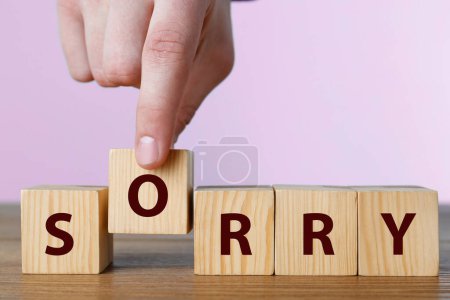 Man putting cube with letter O to make word Sorry at wooden table, closeup