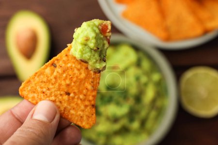 Photo for Woman holding delicious nachos chip with guacamole at table, closeup. Space for text - Royalty Free Image