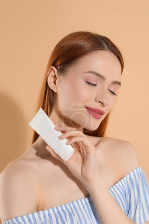 Photo for Beautiful young woman holding sun protection cream on beige background - Royalty Free Image