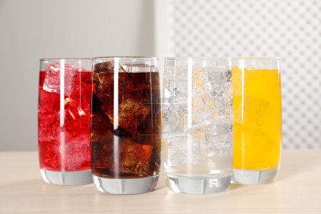 Glasses of different refreshing soda water with ice cubes on white table