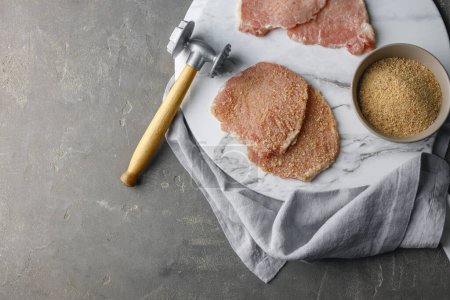 Téléchargez les photos : Schnitzel de cuisine. Côtelettes de porc crues, chapelure avec maillet de viande sur table grise, vue du dessus et espace pour le texte - en image libre de droit