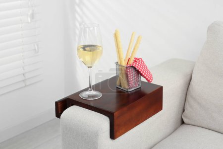 Photo for Glass of white wine and breadsticks on sofa with wooden armrest table in room. Interior element - Royalty Free Image