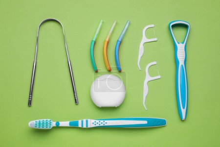 Tongue cleaners and other oral care products on light green background, flat lay