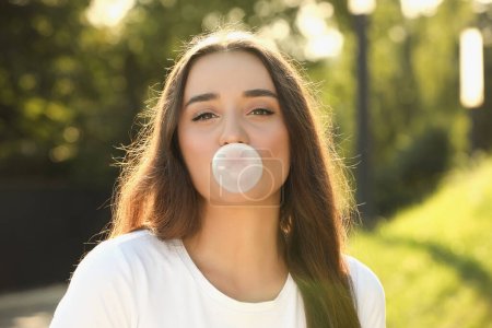 Foto de Hermosa joven mujer soplando goma de mascar en el parque - Imagen libre de derechos