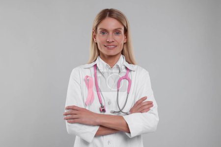 Téléchargez les photos : Docteur avec ruban rose et stéthoscope sur fond gris clair. Sensibilisation au cancer du sein - en image libre de droit
