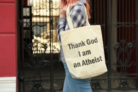 Foto de Mujer sosteniendo bolsa con frase Gracias a Dios que soy ateo al aire libre, de cerca - Imagen libre de derechos